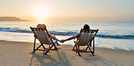 Two people on deck chairs holding hands looking out at the ocean